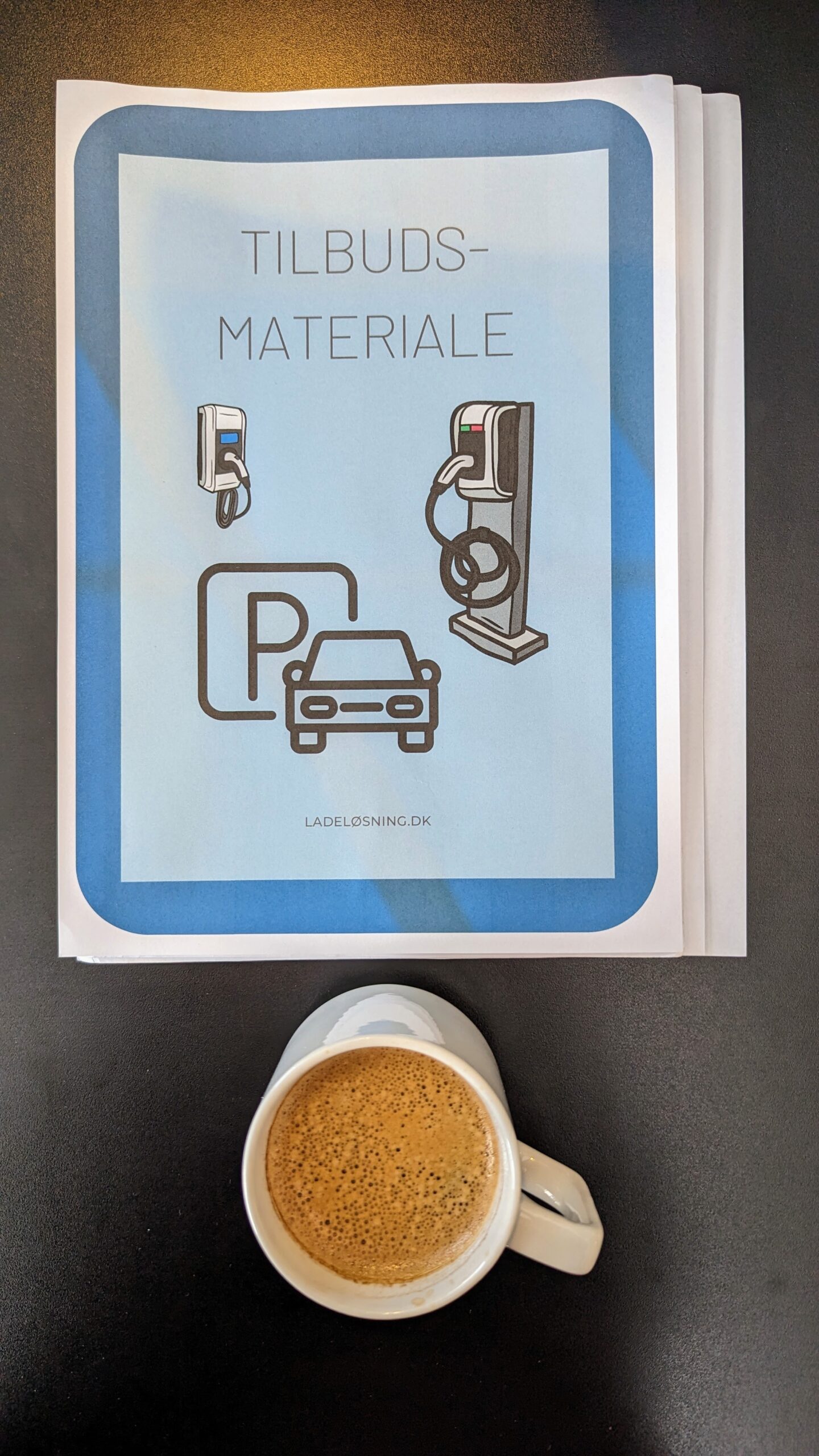 Tilbudsmateriale om ladestandere udprintet på bord ved en kop kaffe.